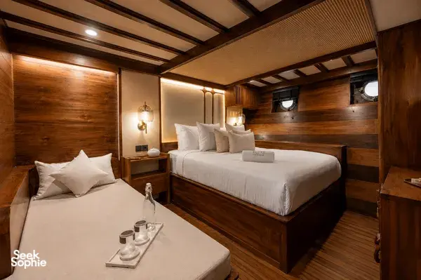 Travass Life new phinisi cabin interior with two twin beds, wooden wall panels, lamps and porthole windows for a Komodo Island trip