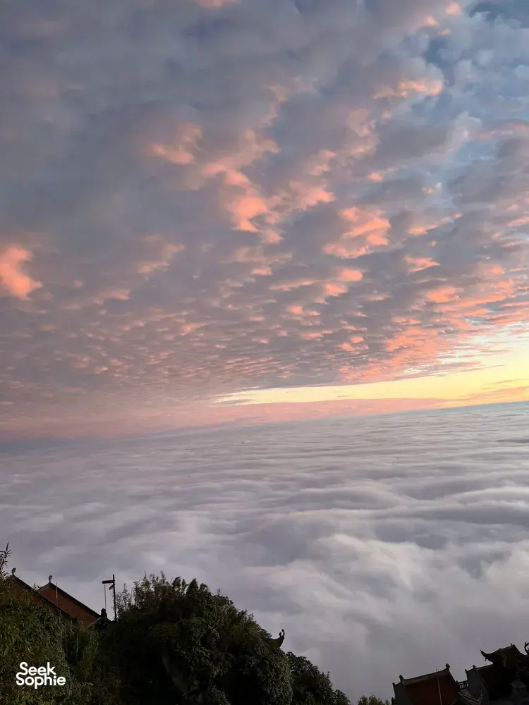Pastel sunrise sky above rolling cloud sea over Sapa, with rooftops in the foreground from Mt Fansipan