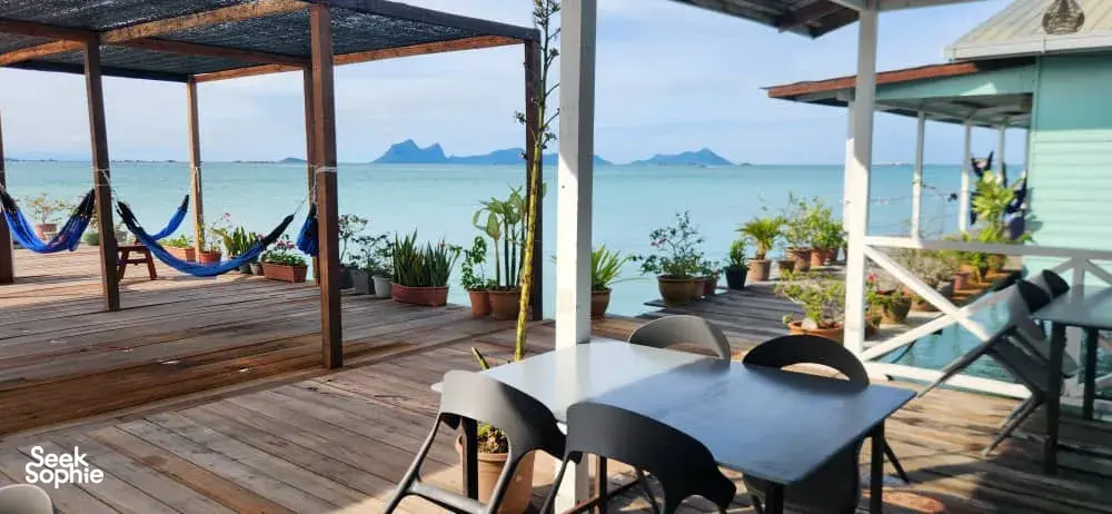 Meja makan dan buaian gantung di dek kayu banglo air di Semporna, dengan laut terbuka dan pulau-pulau di kejauhan