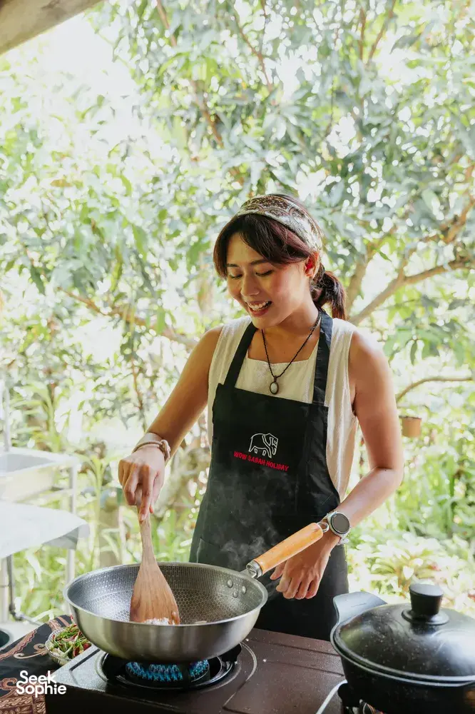 Local Sabahan family cooking in Kota Kinabalu, Borneo—stirring ingredients in a large wok over an outdoor stove