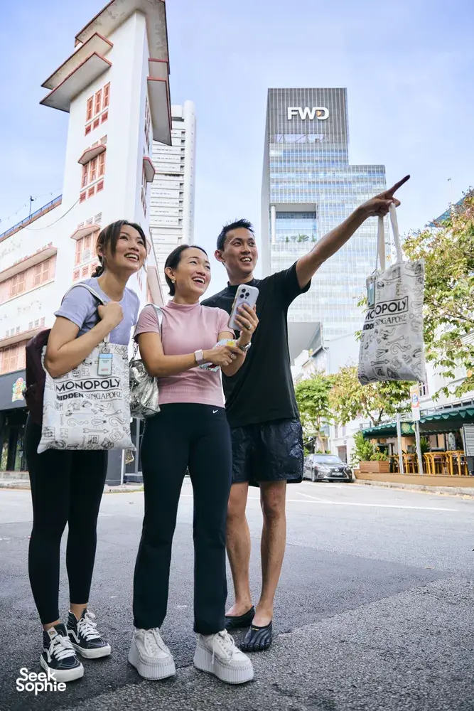 一群人在新加坡河畔的街头参与现实版大富翁游戏,摆姿势合影并手拿托特包——新加坡小众宝藏体验