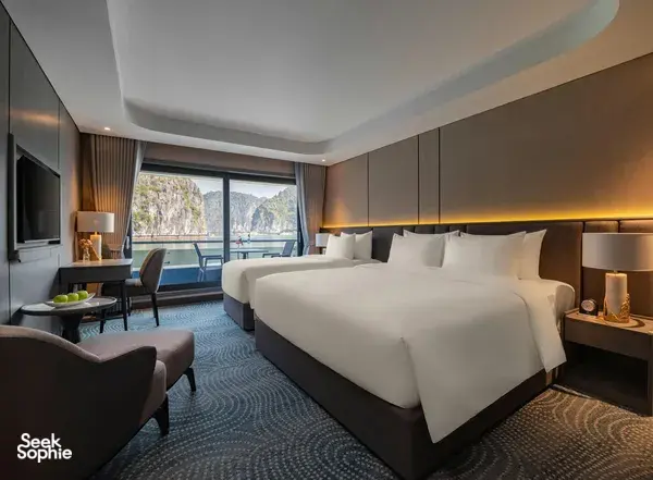 Tulip Cruise bedroom with neatly made double bed, bedside lamps and lounge seating, plus panoramic sea-view window in Halong Bay