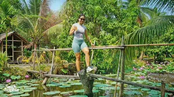 Traveller posing on a wooden bridge beside a lily pond on Mekong Island during a bike tour from Ho Chi Minh City