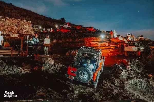 Headlights glow as off-road jeeps ferry travellers over rocky ground at dusk on the Bali slopes of Mt Batur