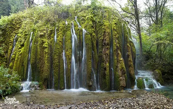 Multi-tier waterfalls in Shangri-La tumbling through a green forest, with moss-covered cliffs and misty water