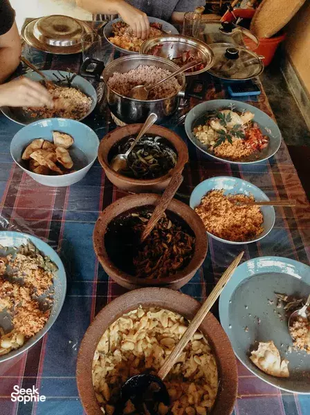 Shared communal dinner in Sri Lanka with multiple bowls of dishes and serving pots, as hands reach across a wooden table