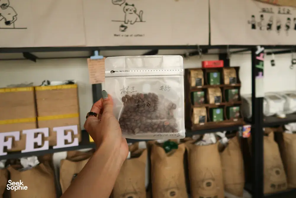 Hand lifting a bag of roasted coffee beans in a family-run coffee workshop in Lijiang, part of a specialty cupping