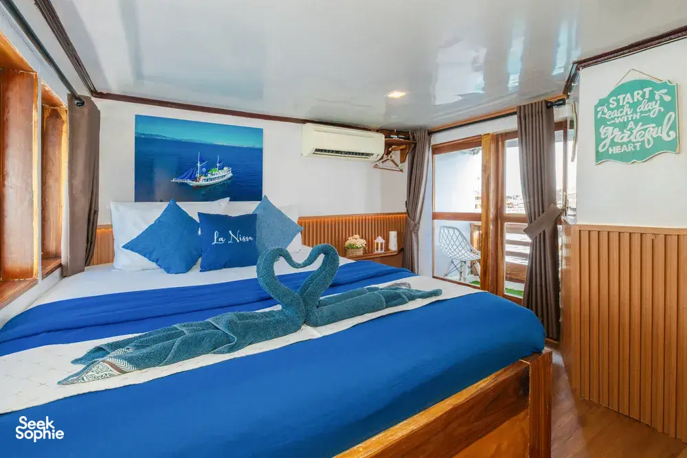 La Famille cabin with blue-and-white bedding, a folded towel lizard and a chalkboard welcome note by the window, Labuan Bajo