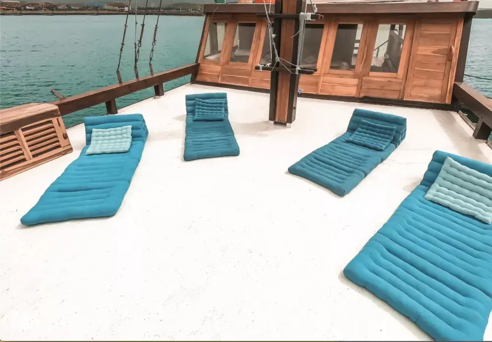 Sunlit upper deck with neatly arranged blue cushions and railings, on a phinisi boat sailing for Komodo Island