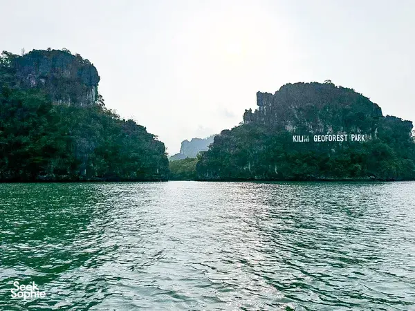 Kilim Geoforest Park sign on karst cliffs across the water, viewed from a Langkawi cruise boat