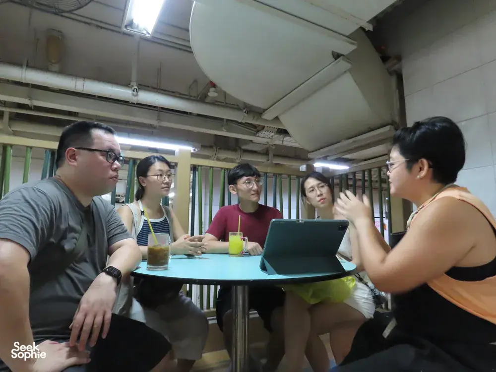 在新加坡室内餐馆厨房里,小团体正围着笔记本电脑听取关于粤式鱼料理与小贩美食之旅的简报