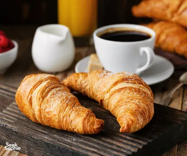 Croissant bermentega di atas papan kayu dengan secawan kopi hitam di latar semasa sesi Bake Croissants + Coffee di Singapura