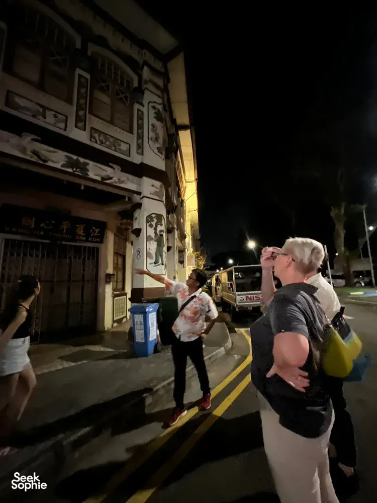 Guide gesturing along a dim Geylang street during Indie Singapore Tours’ private night walk, with visitors looking on, Singapore hidden gems