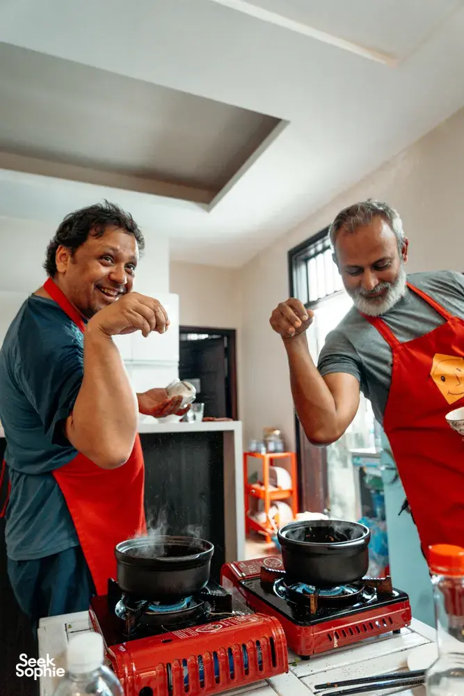 在会安 Jolie Cooking Class 的越南家常烹饪体验中，两位系着红围裙的人正在炉边搅拌锅里的食材