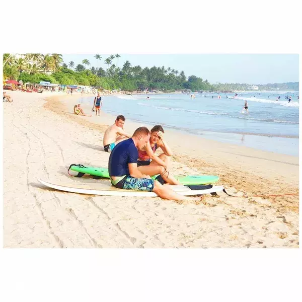 Learner surfers lying on green boards on Weligama beach, with a palm-lined coastline in view at Surf N' Lanka