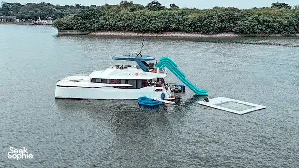 MS Eternity twin-deck catamaran floats on calm water beside a tree-lined Singapore shoreline, prepared for the 4-hour Lazarus trip