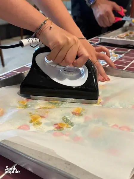Hands heat-sealing reusable food wrap material with an iron during Agrihome sustainability workshops in Singapore