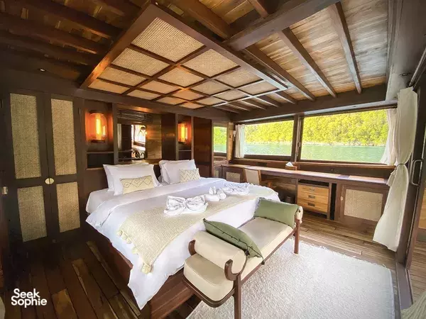 Romantic luxury cabin bed inside a traditional overwater lodge in Raja Ampat, with large windows and sea view