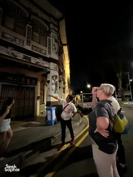 Guide gesturing along a dim Geylang street during Indie Singapore Tours’ private night walk, with visitors looking on, Singapore hidden gems