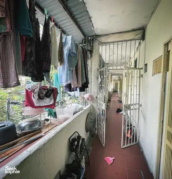 Lorong sempit di perumahan komuniti Hanoi dengan pintu berjeriji, pakaian yang digantung, dan kasut di sepanjang koridor.