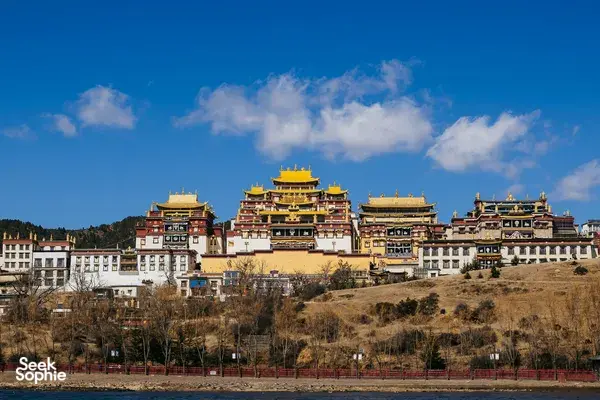 Shangri-La hillside temple complex with layered golden roofs and ornate red-and-white ramparts under a clear blue sky