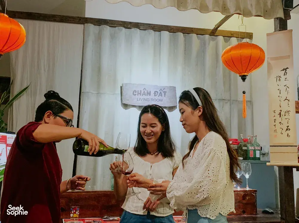 Tamu di Chan Dat Living Room, Hoi An, menuang dan mencicipi anggur merah sambil tersenyum dengan gelas di tangan di ruangan bercahaya lentera