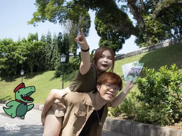 Two people pose with clue cards and point towards the garden while progressing in a Puzzle Hunt at Fort Canning, Singapore