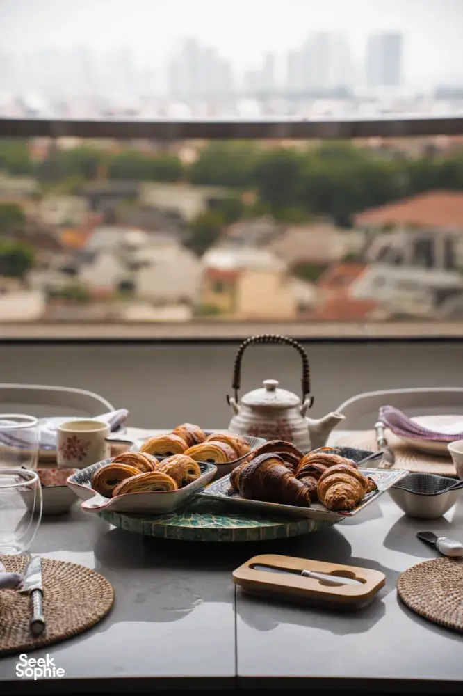 Croissants arranged on serving trays with tea set on a balcony table overlooking Singapore at a French Cooking Lab bake session