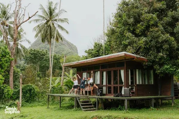 Eco-lodge cabin on stilts with guests on the veranda amid palms and jungle greenery near Khao Sok National Park
