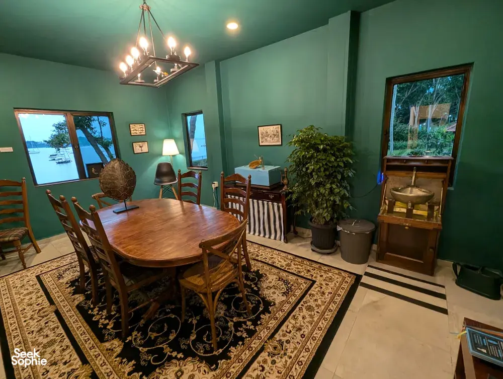 Dining room with a wooden table and chairs, green walls and windows framing the sea at The Unexpected’s Singapore farmstay by the sea