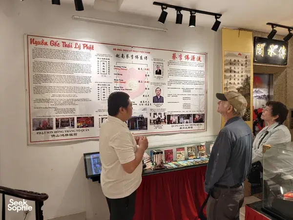 People discussing a Kung Fu and lion dance exhibition board in a Ho Chi Minh City heritage display room, with brochures on a table