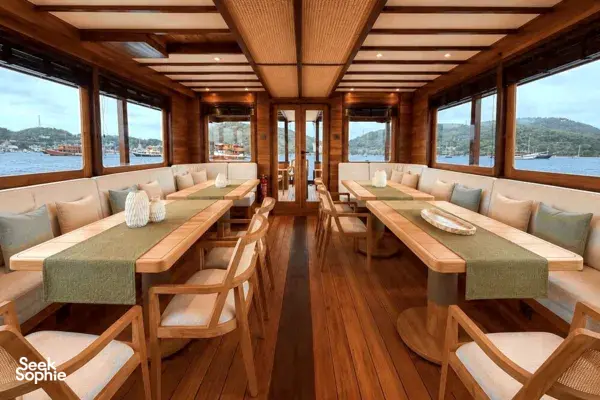 Spacious phinisi lounge with bench seating and long tables, set above the waves on a Komodo Island shared trip