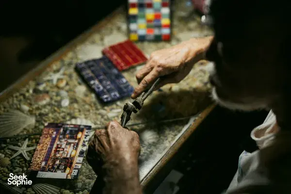 Tangan memperlihatkan kartu vintage dan tekstil di ruang arsip tersembunyi untuk kisah apartemen sewa Hidden Heritage dan hidden gems Singapura