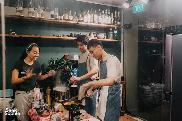 Three people in aprons stirring pots and tossing pasta in Singapore during private pasta making — workshops in Singapore
