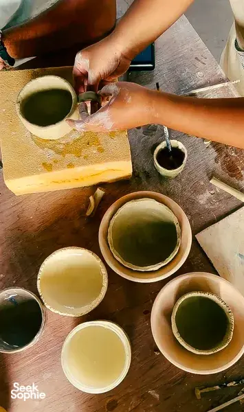 Hands painting and shaping small ceramic bowls with pale green glaze at Ilham Ceramic Studio in Langkawi