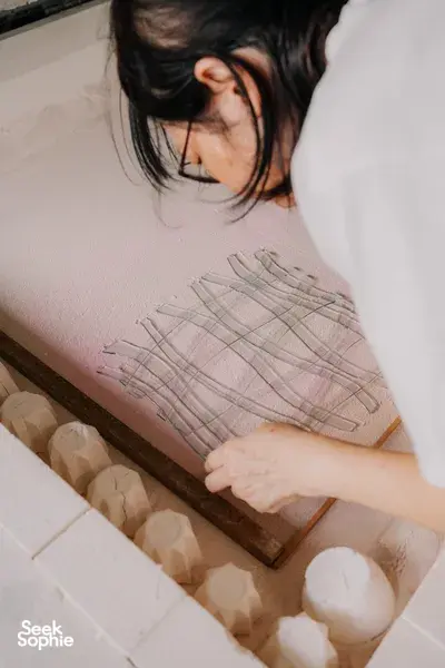 Participant’s hands placing glass tiles on a grid template at Art Glass Centre in Singapore — workshops in Singapore