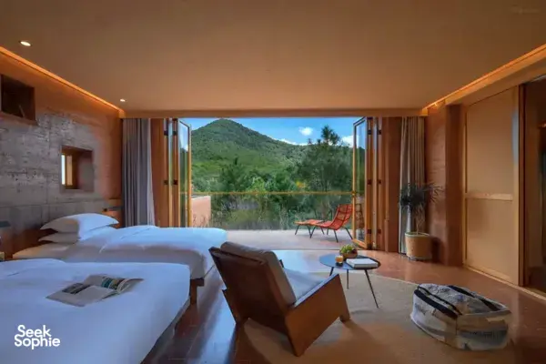 Guest bedroom at Linden Centre eco retreat with beds and open doors to a terrace, where a green mountain view fills the scene