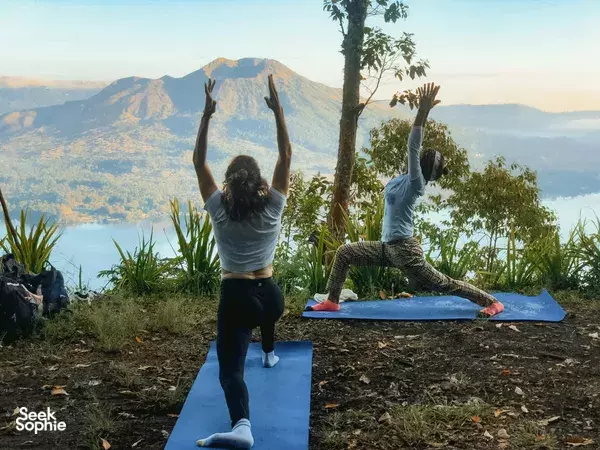 Pranasanti Yoga private session outdoors, participants stretching on mats with arms raised over a Bali valley in Ubud