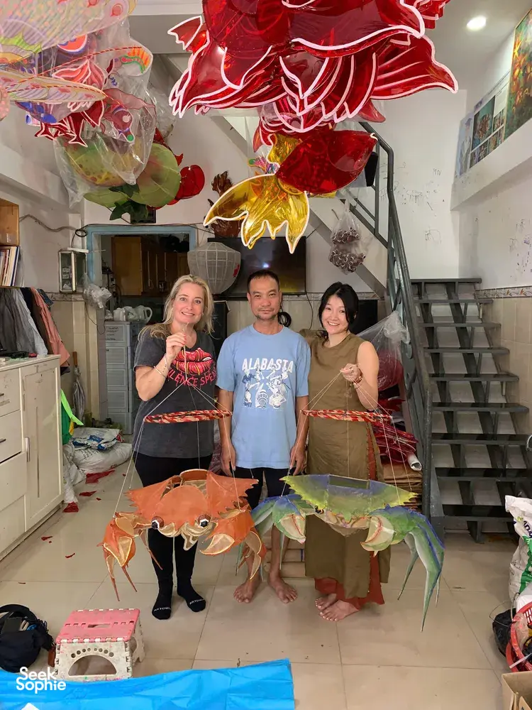 Three visitors posing with handmade red and green paper kite lanterns in a Saigon craft shop led by Viet Awesome Tours
