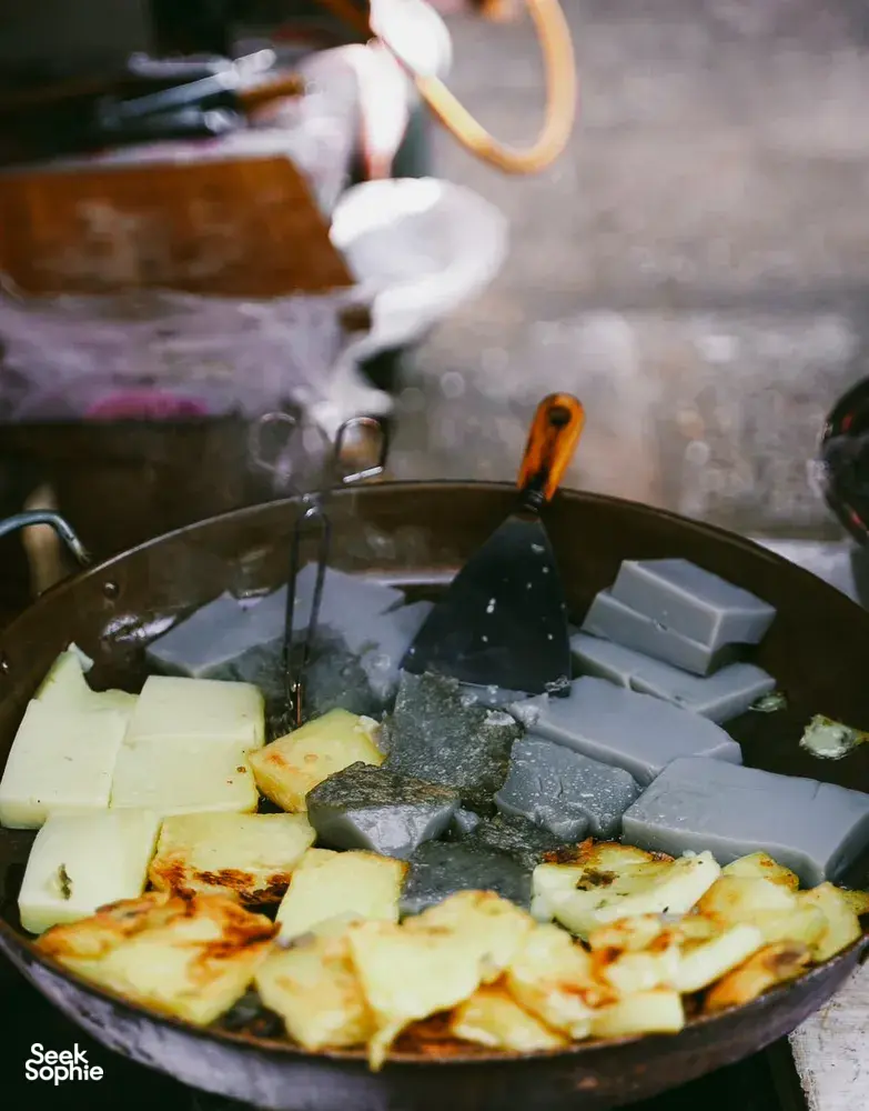 Sizzling wok of fried tofu and batter in a smoky Lijiang stall, capturing the flavours behind a local food hunt