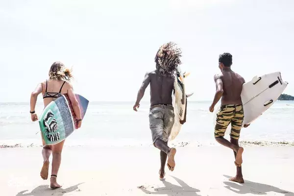 Surfers running along Weligama beach with surfboards toward the sea for a 6D7N experience at The Green Rooms surf camp