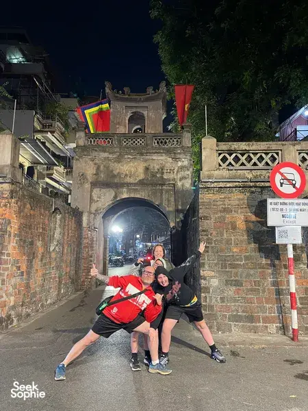 Travellers posing in a narrow illuminated laneway beneath an old stone arch during a Hanoi night food experience