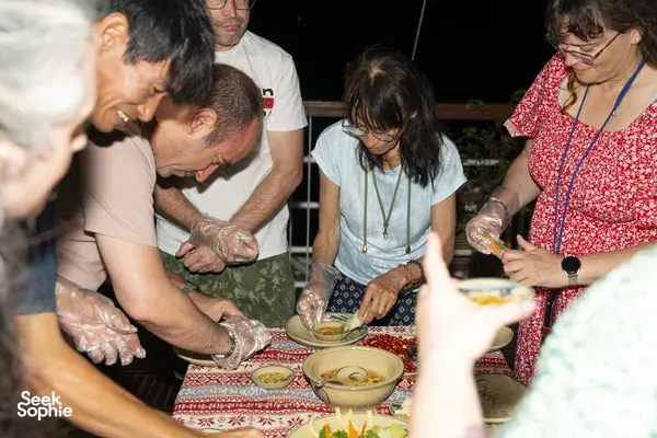 Guests at night on a cruise table wash and prepare seafood in bowls, sharing the evening meal during the Cat Ba experience