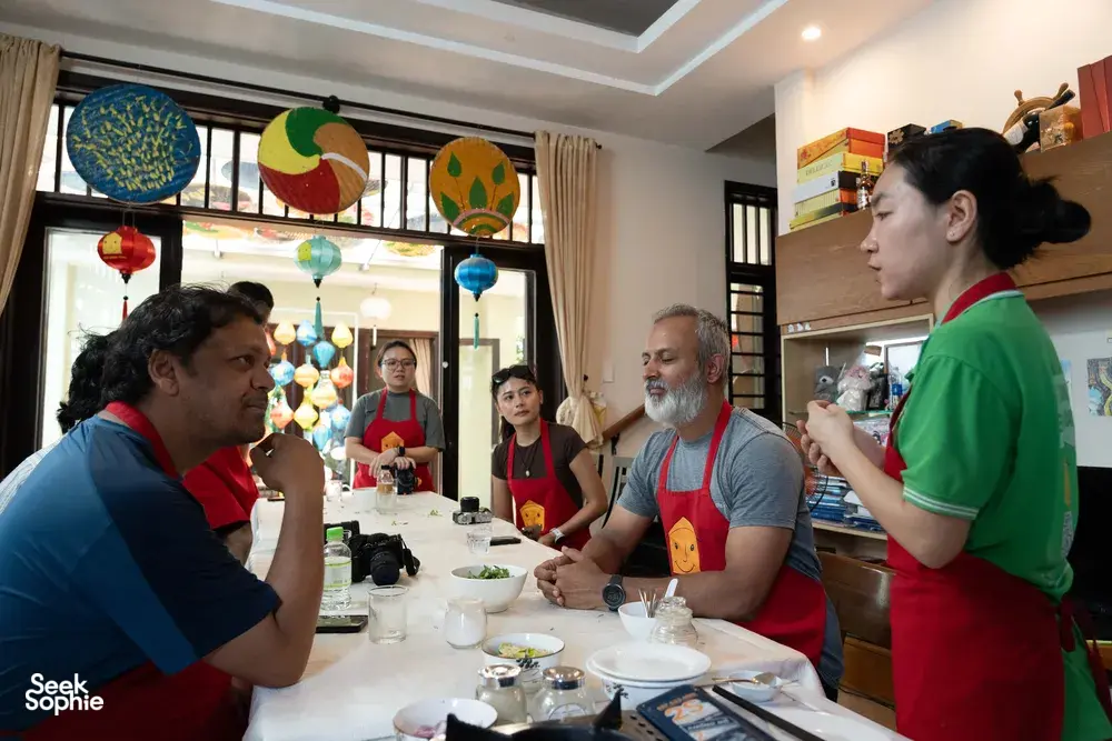 客人们围坐在会安 Jolie Cooking Class 的餐桌旁，在家庭式厨房里学习制作越南菜