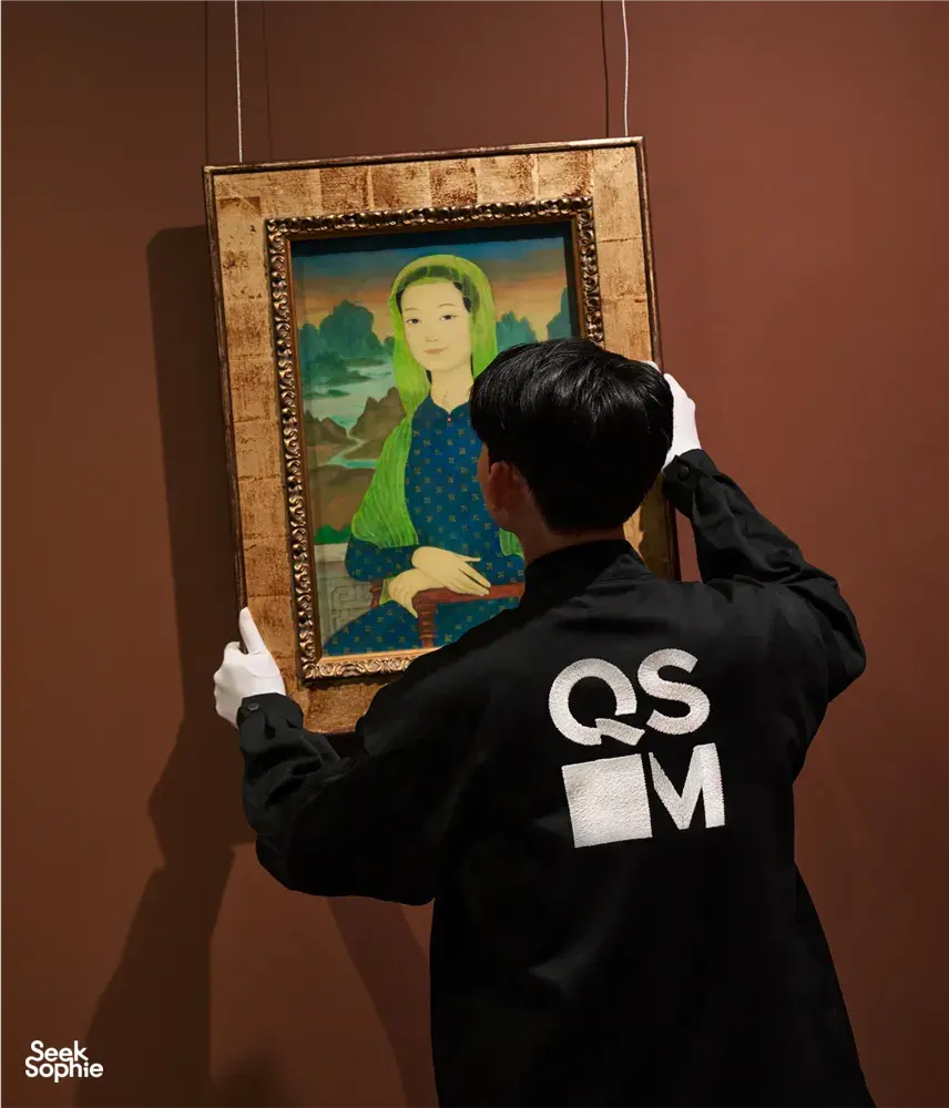 A guide from Quang San Art Museum adjusts a framed Vietnamese portrait for visitors during an art tour in Ho Chi Minh City