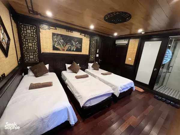 Cozy wooden cruise cabin in Cat Ba with three neatly made single beds, patterned wall panels and lounge-style lighting