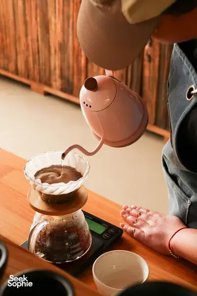 Hands pouring coffee from an electric kettle into a cup during a small-batch brew at Seeker Yunnan Coffee Estate, Lijiang