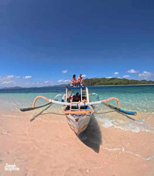 Bale Laut Tour speedboat on a sandy Gili Islands shoreline in Lombok, with snorkellers relaxing on the boat deck.
