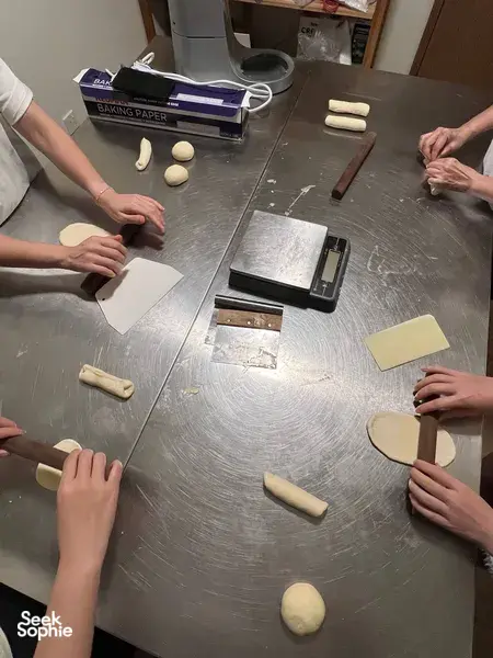 Baker hands pressing and folding shio pan dough shapes on baking paper beside tools during workshops in Singapore