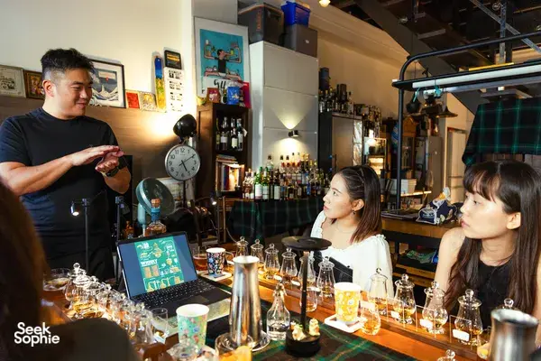 Small-batch whisky tasting in a hidden home bar in Singapore, a host pours for guests at a table of sample glasses and bottles
